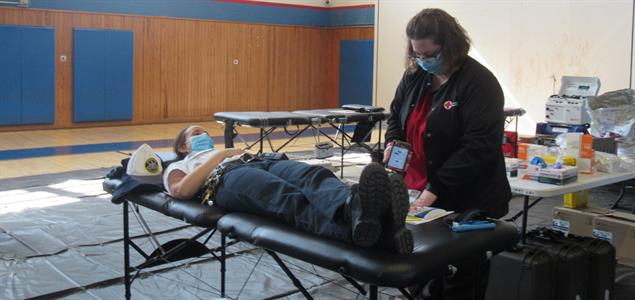 A person lays down donating blood with a nurse standing beside