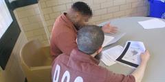 Two inmates sit at a table completing school work