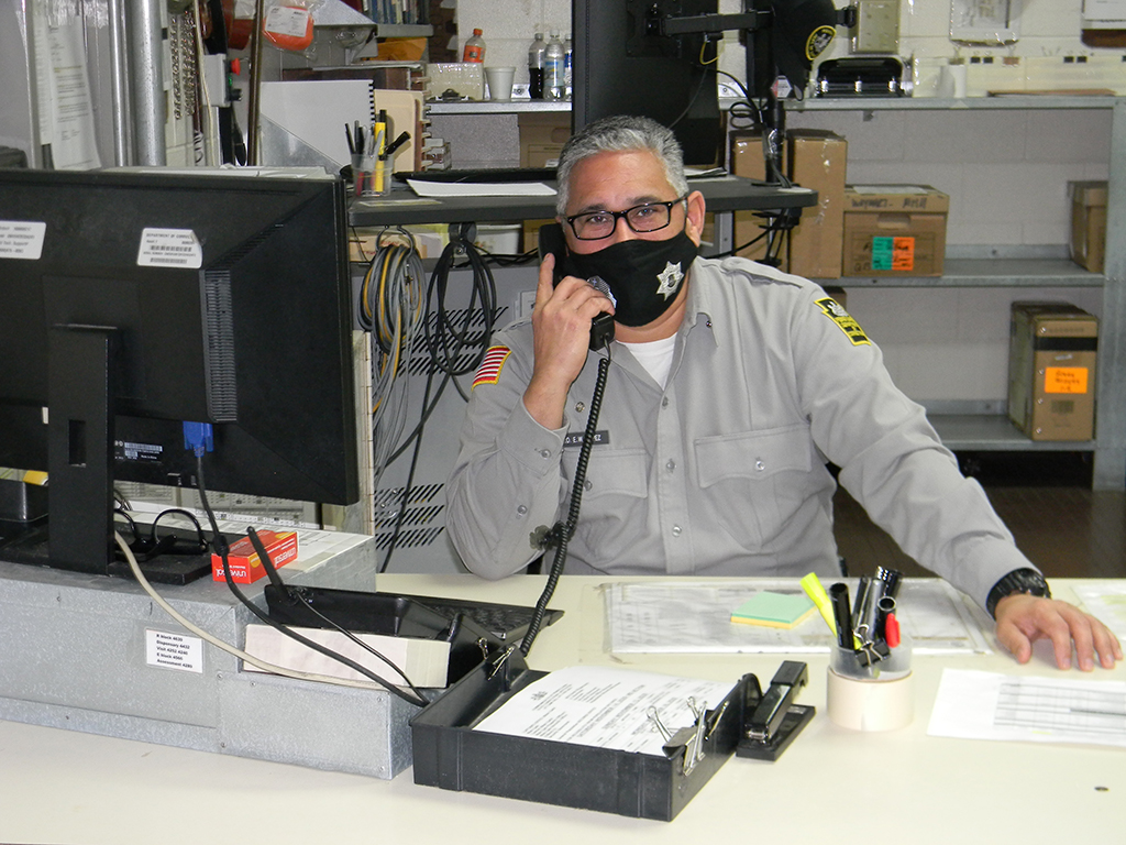 A corrections officer at his desk answers the phone