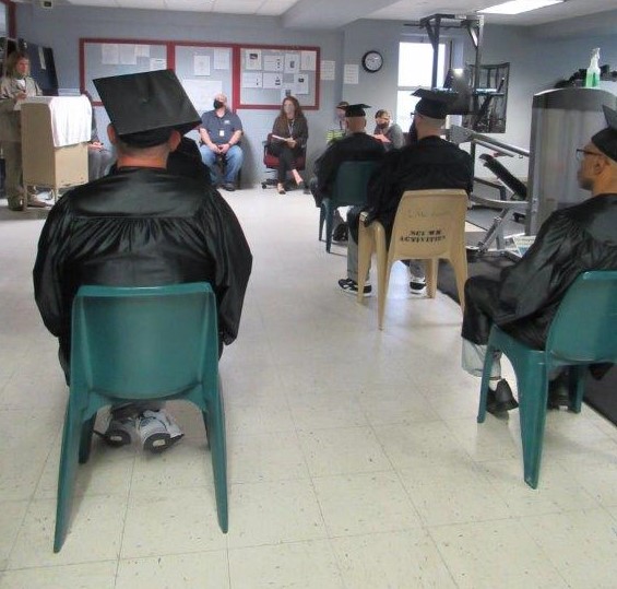 Inmate graduates sit in a gym during a ceremony