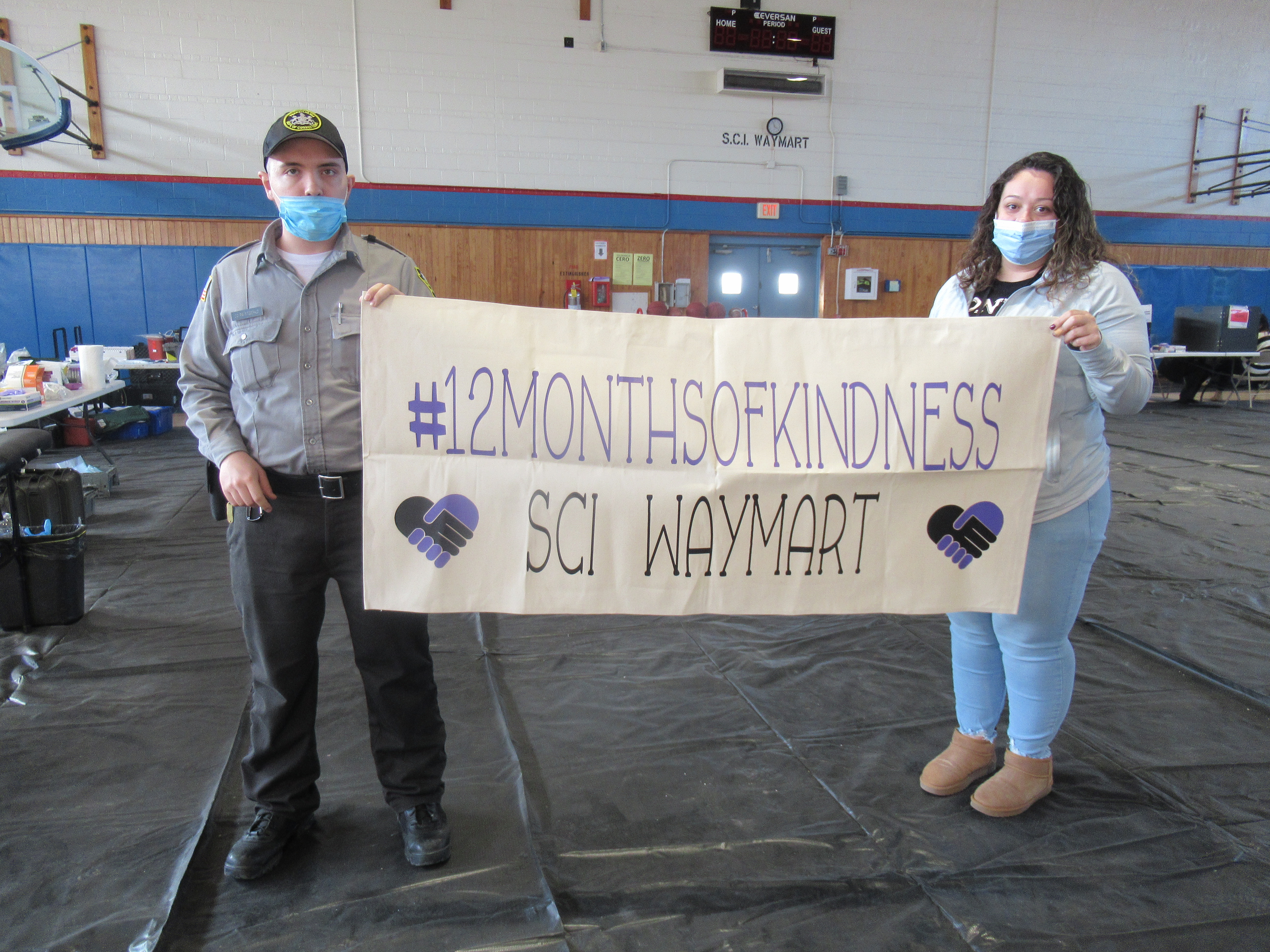 Two people hold a sign that says #12MonthsofKindness