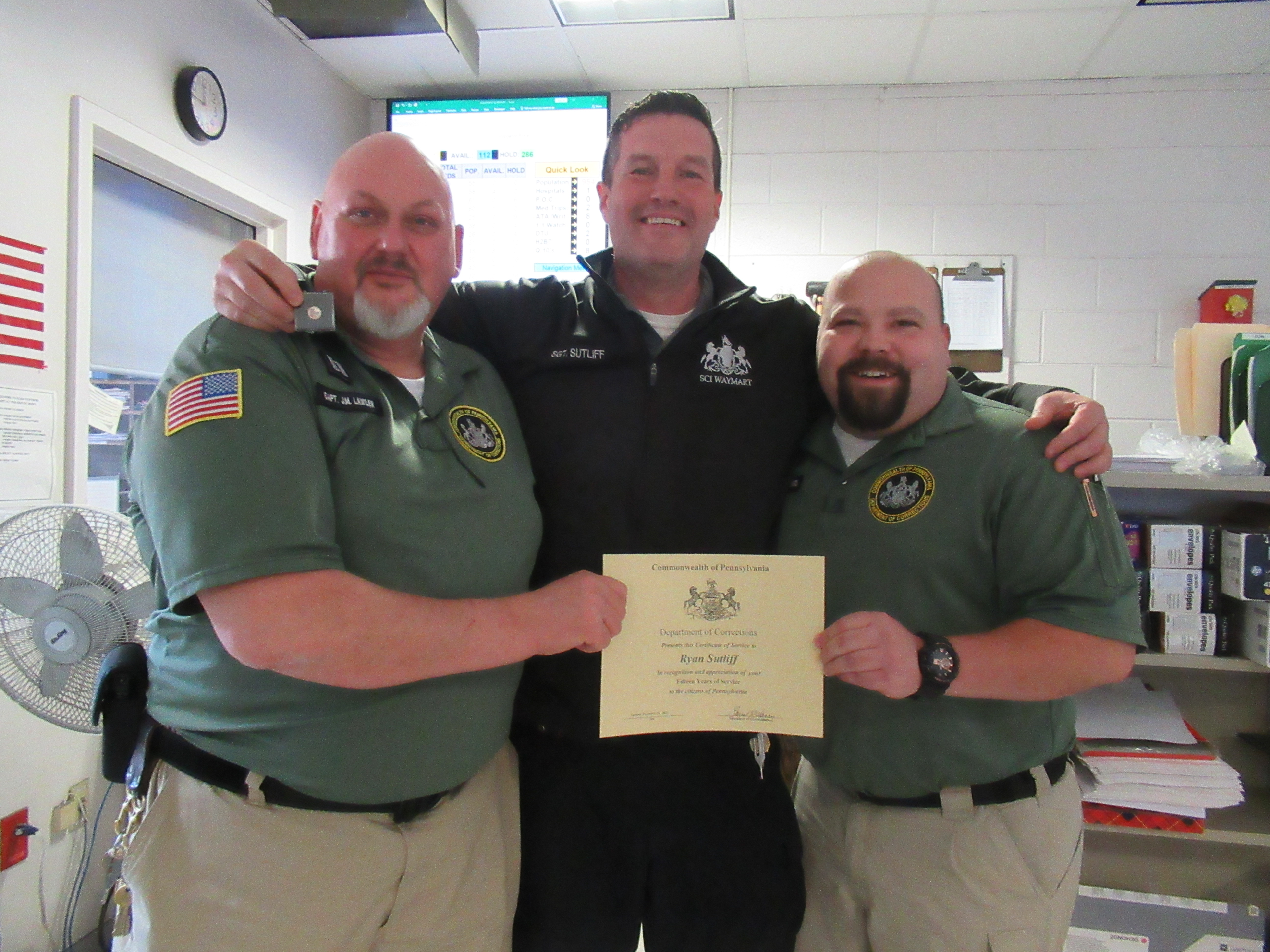 Sgt. Ryan Sutliff holding a pin while surrounded by Captain J. Lawler and Lt. C. Edwards, who are holding a certificate.